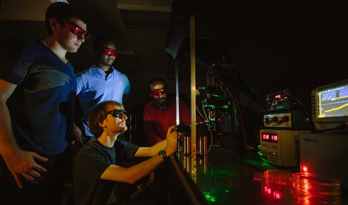 Philip Vendola ’16 (left) and Wesley Pierre ’16 (center, top) watch as Blades (below) and Rotkin (right) use a Raman microscopy system to find and quantify the properties of a single layer of graphene that has been carefully transferred onto a soft-matter