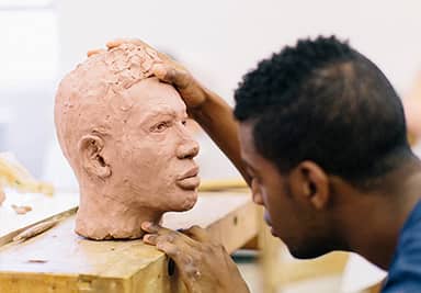 A student sculpting a head made of clay